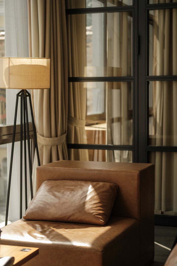 A serene modern living room with leather armchair, floor lamp, and elegant curtains.